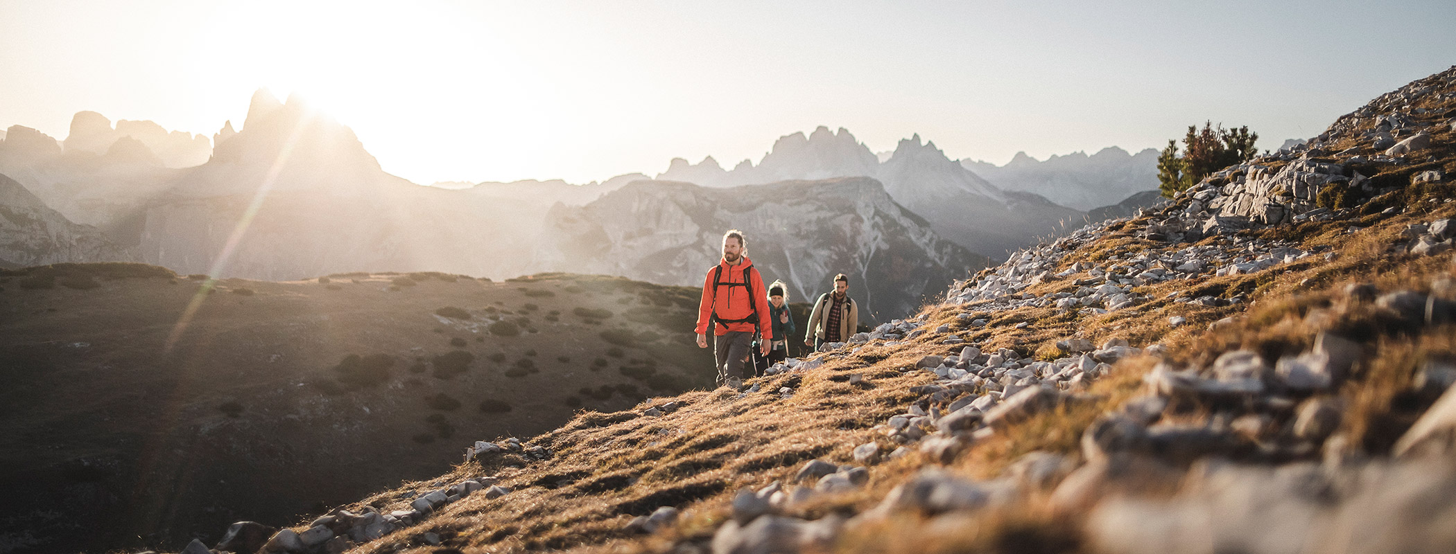 Three hikers in the Dolomites walking along mountain meadows in autumn - Laurin's