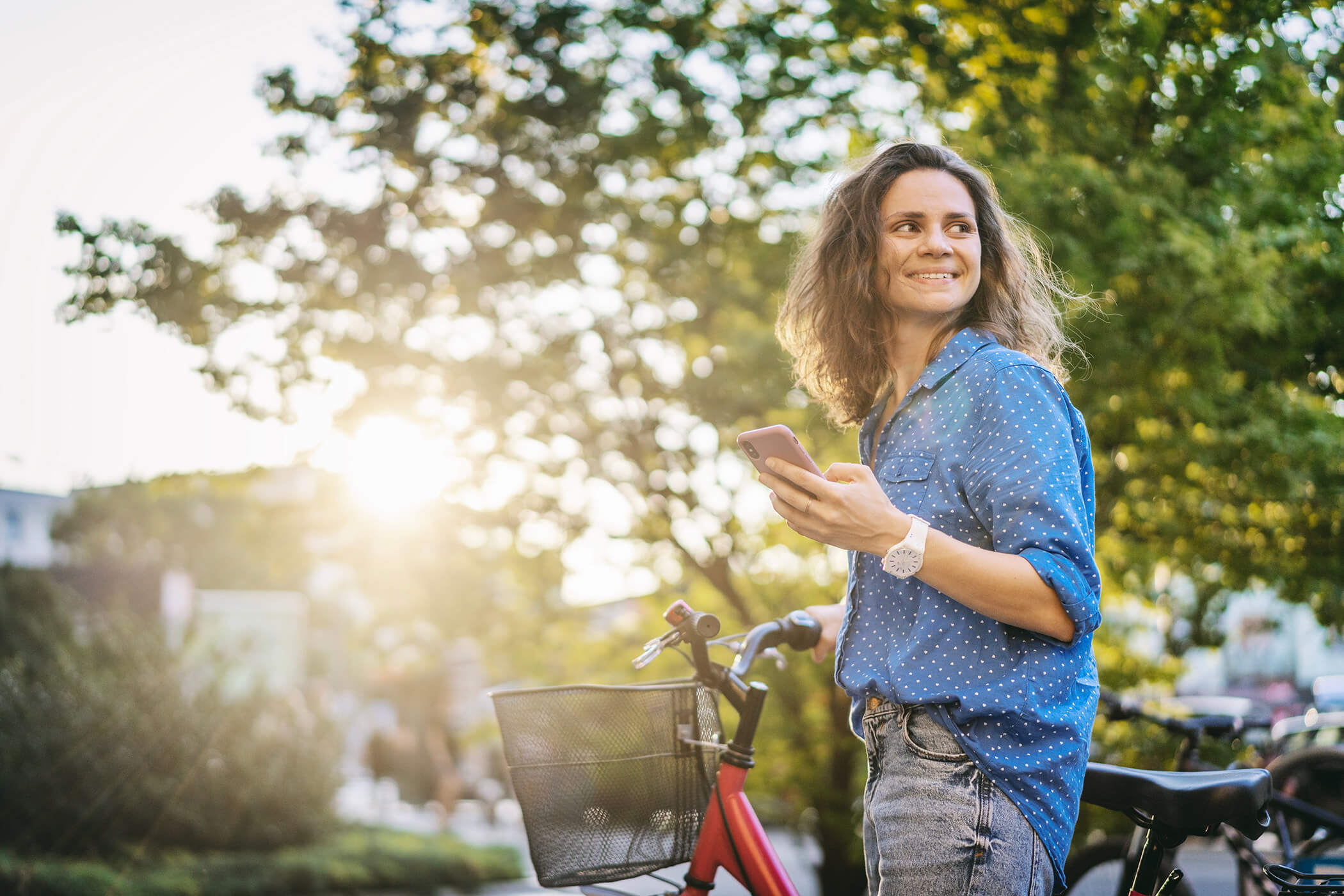 Una donna tiene la bicicletta in una mano e il cellulare nell'altra e sorride - Laurin's